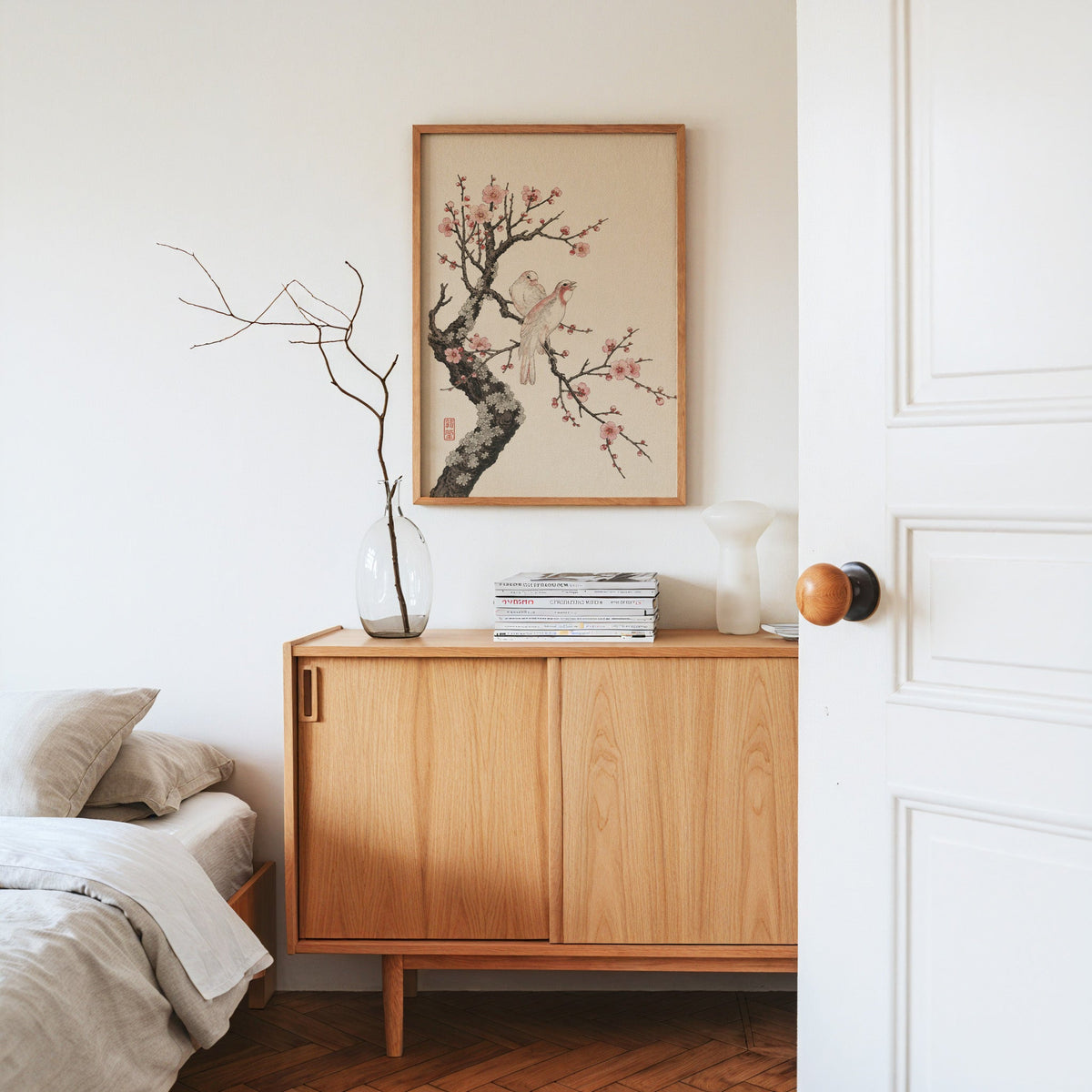 two birds on pink blossom branch print in an oak frame above an oak sideboard in a bedroom with linen bedding