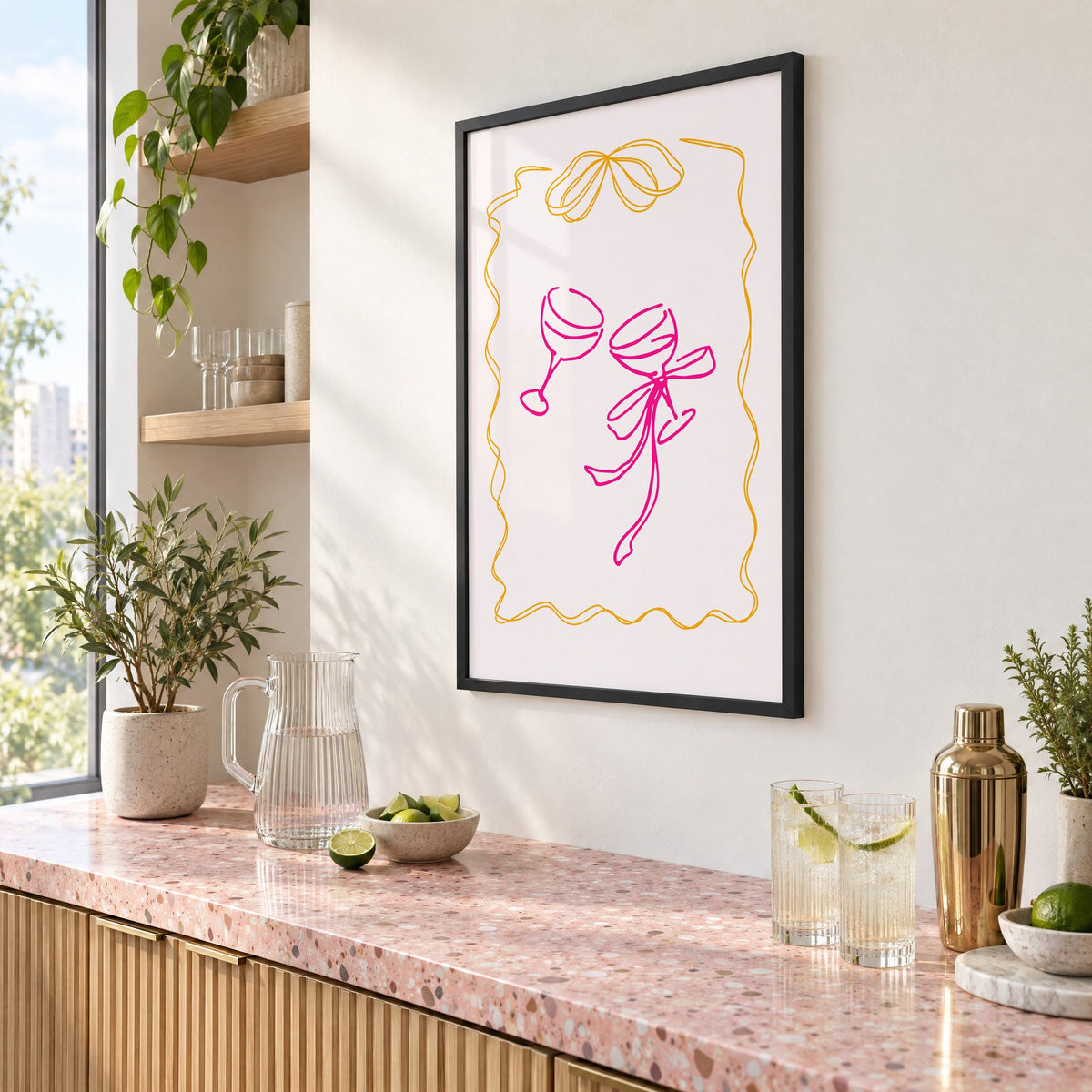 Two coupes pink bow ribbon frame print in a black frame above a pink terrazzo cocktail counter with limes, seen at an angle