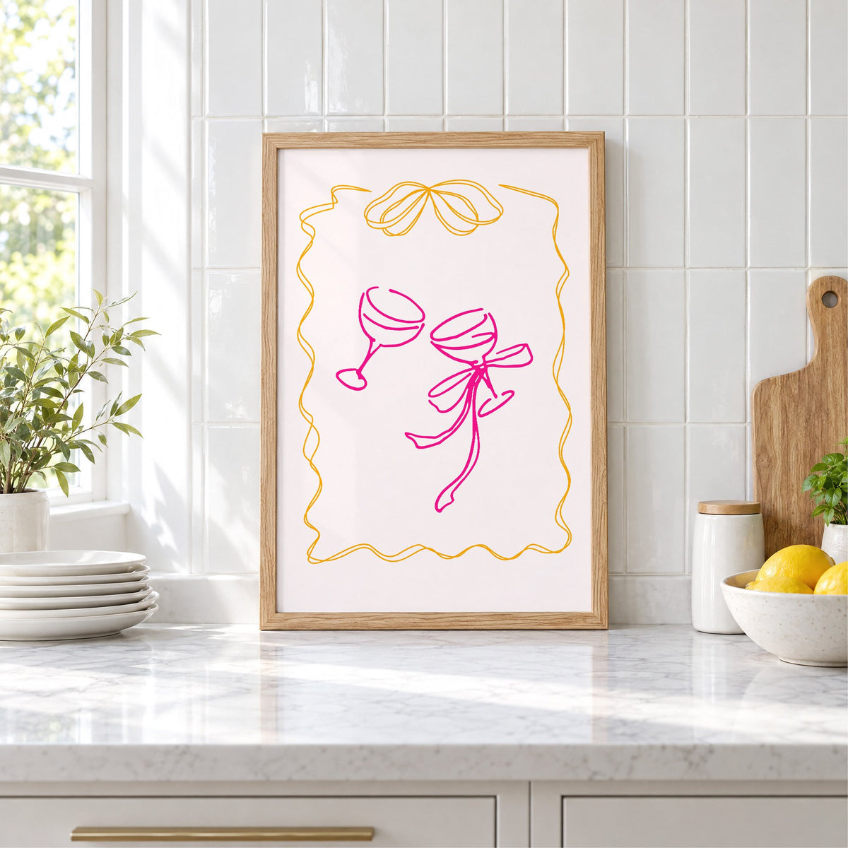 Two coupes pink bow ribbon frame print in an oak frame leaning on a marble counter by white tiles and lemons