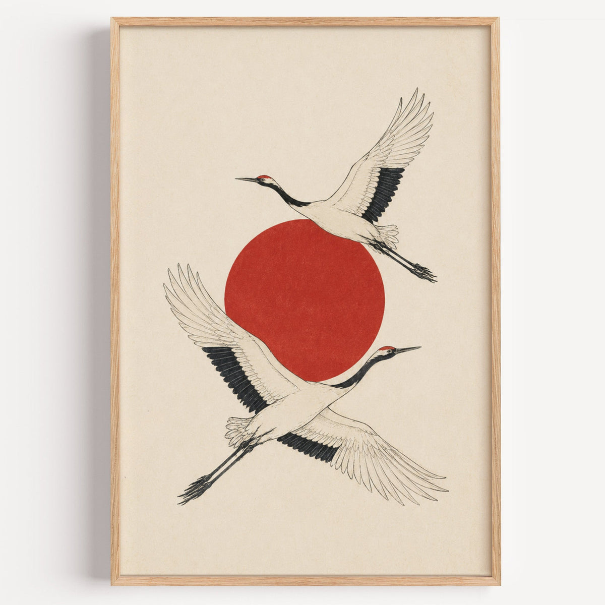 two cranes crossing a red sun print in a light oak frame on a plain white wall