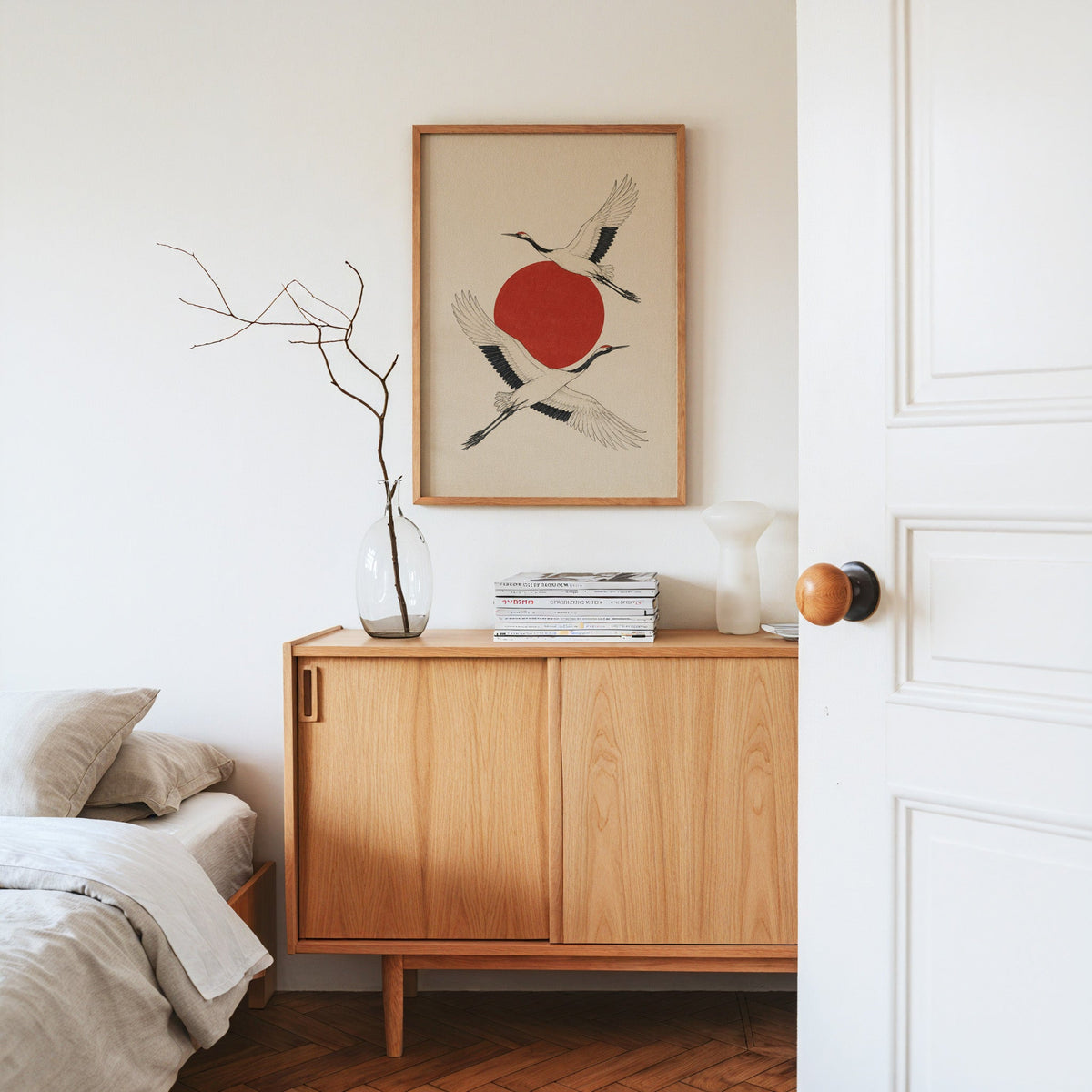 two cranes crossing a red sun print in an oak frame above an oak sideboard in a bedroom with linen bedding