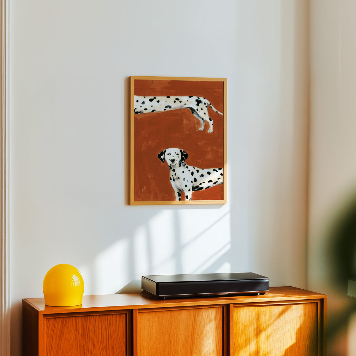 Dalmatian dog wall art print in a light oak frame above a teak sideboard with a yellow lamp