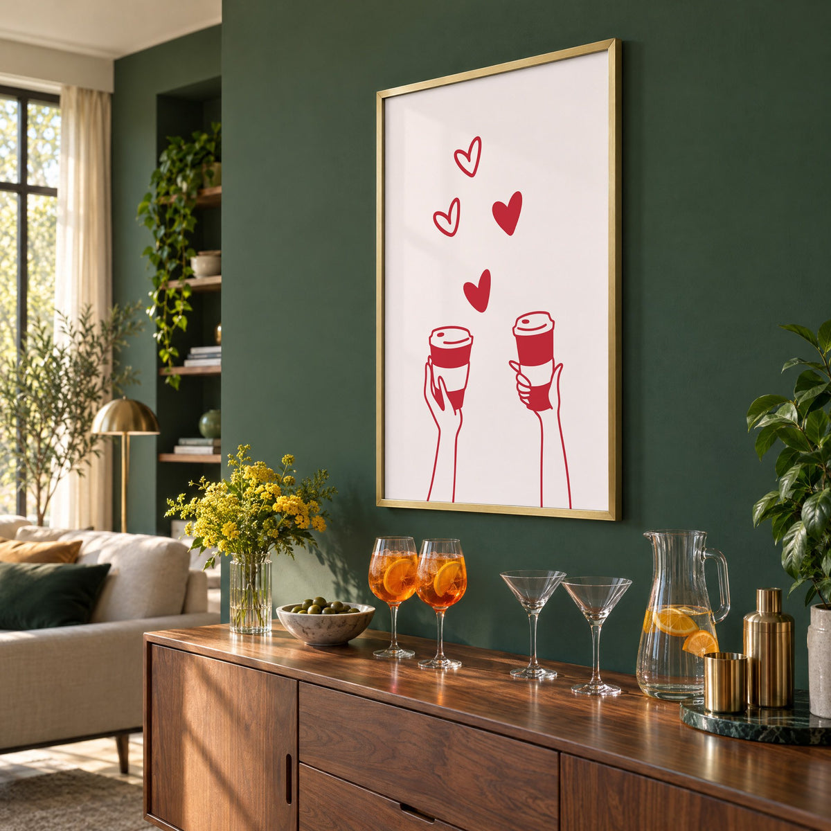 Two hands coffee cups and hearts red line print in a brass frame on a bottle green wall above a sideboard with spritz and martini glasses, seen at an angle