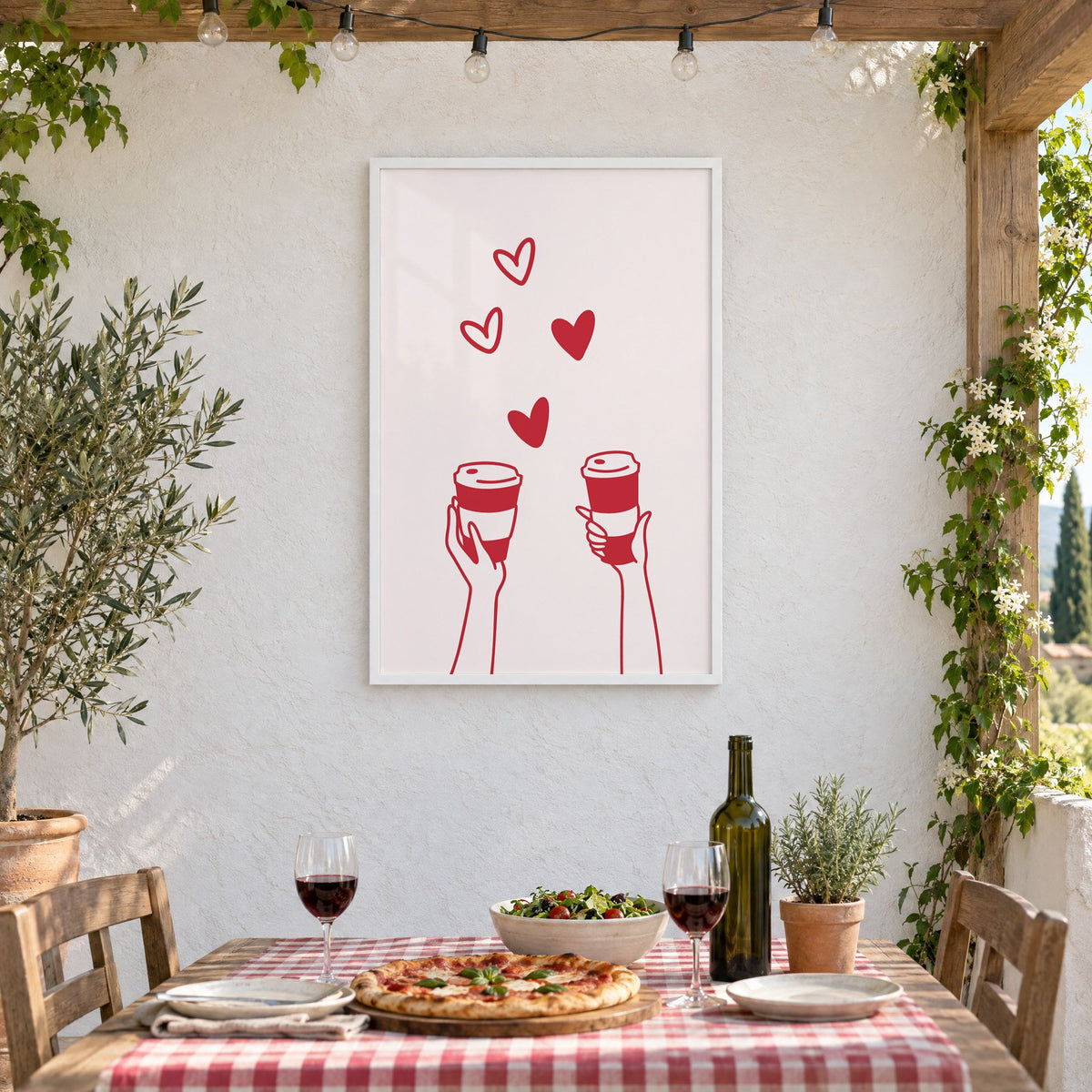 Two hands coffee cups and hearts red line print in a white frame on a stucco wall above a checked-cloth table with pizza and red wine