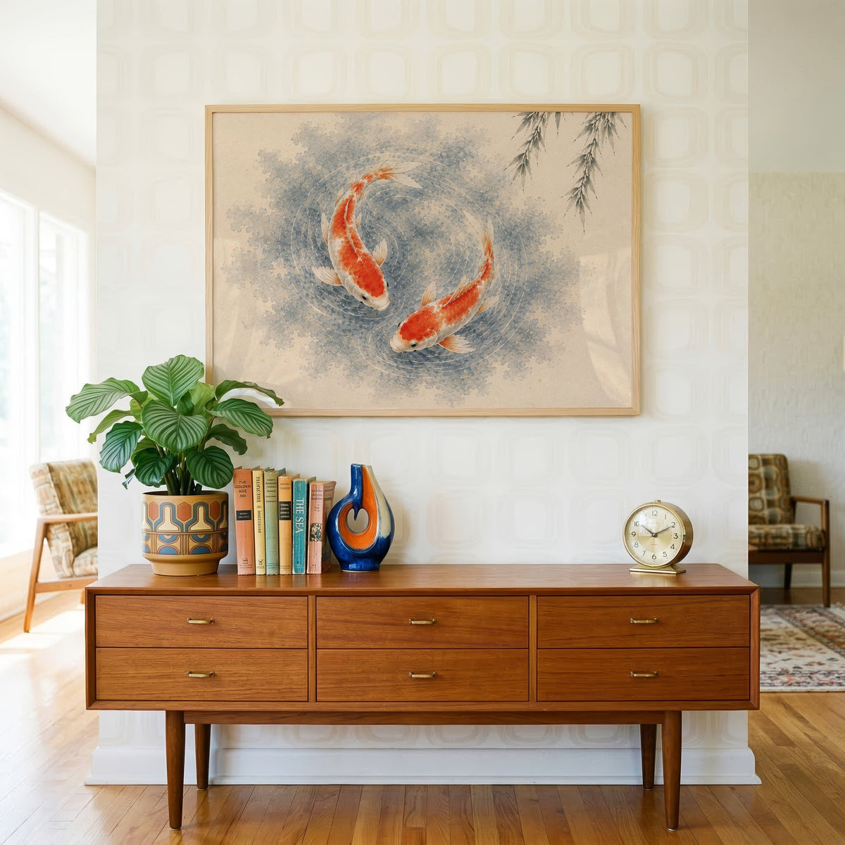 Two koi circling under a willow print in a light oak frame above a teak credenza with books and a brass clock