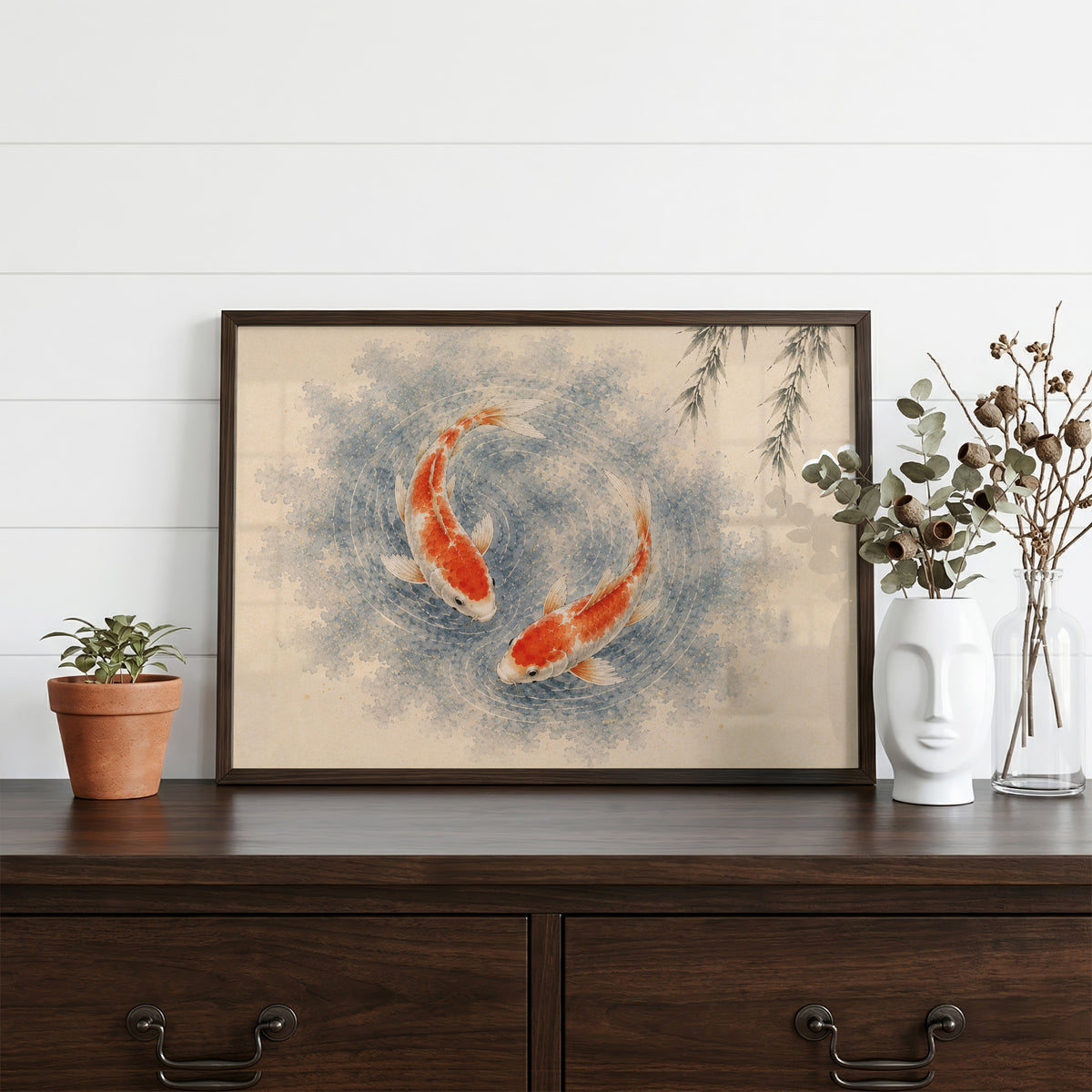 Two koi circling under a willow print in a dark walnut frame on a dark wood dresser beside a white face vase