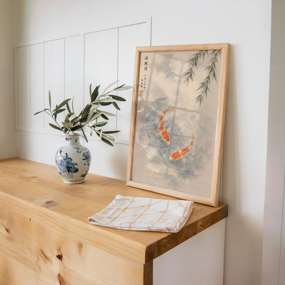 two koi with willow and moon print in a pine frame on a wooden counter beside a blue and white porcelain vase