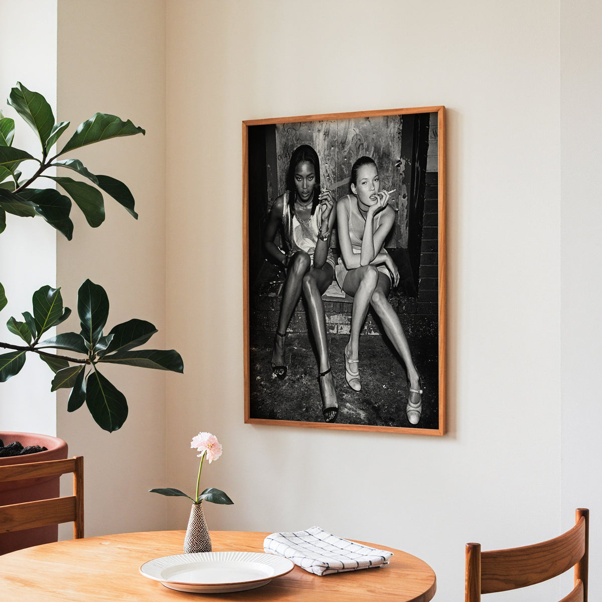 Two women seated on brick doorway steps print in a teak frame above a round wooden dining table