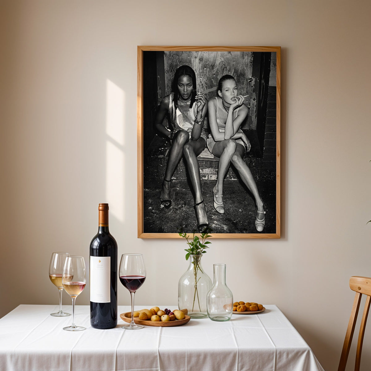 Two women seated on brick doorway steps print in an oak frame above a table set with red wine and glasses