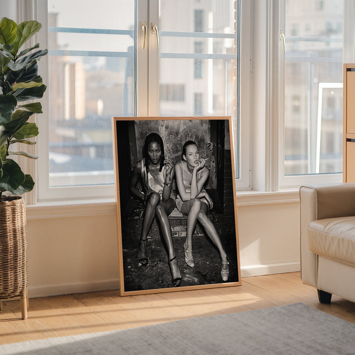 Two women seated on brick doorway steps print in an oak frame leaning on the floor beside a fiddle leaf fig