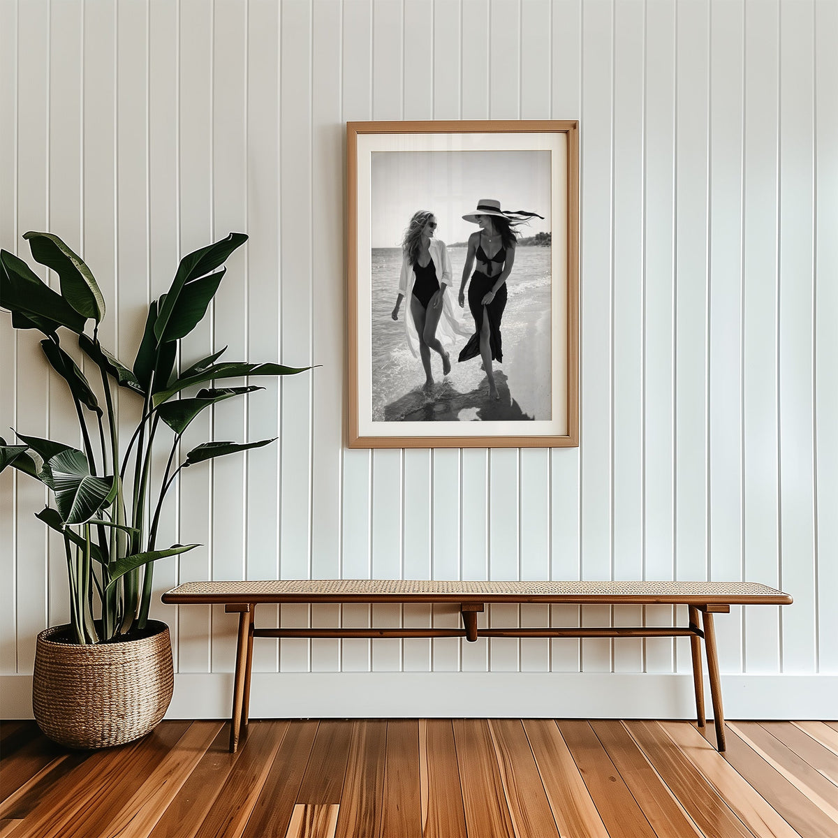 Two women walking the shoreline and laughing print in a wood frame with a white mat above a cane bench