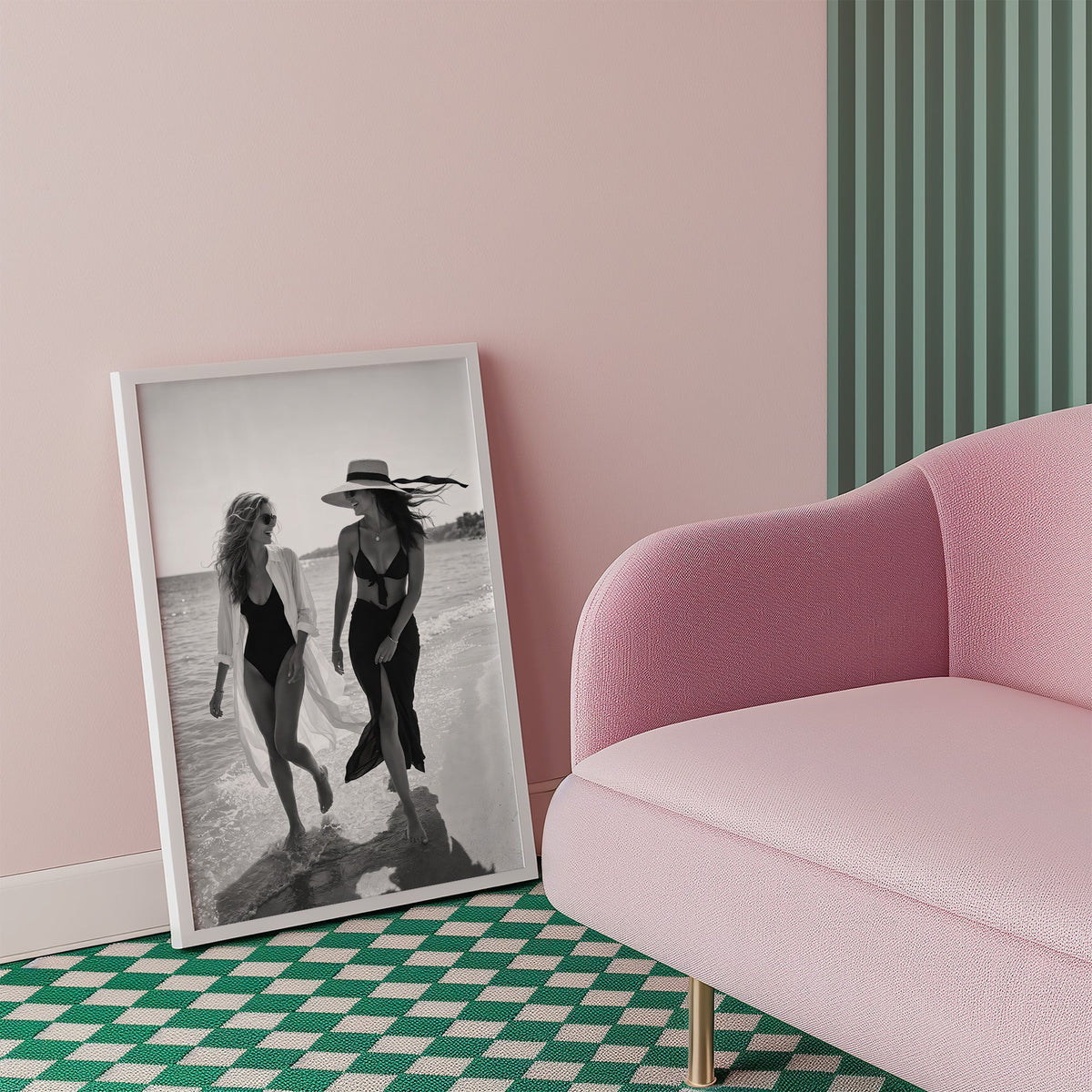 Two women walking the shoreline and laughing print in a white frame beside a pink armchair on a checkered floor