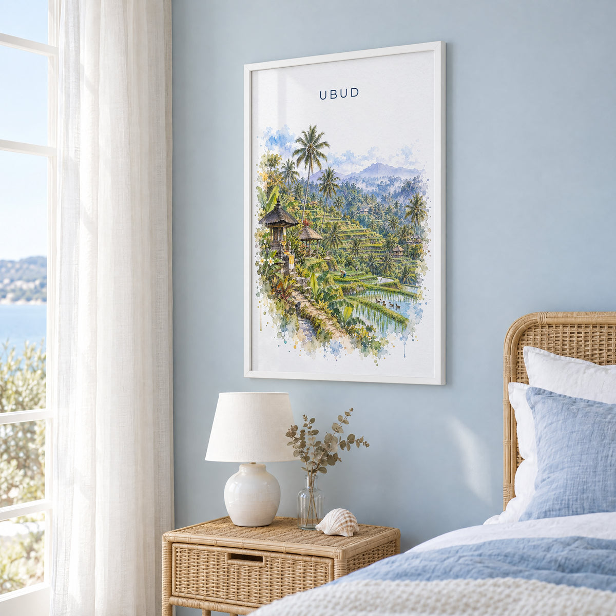 Ubud watercolor print in a white frame on a pale blue wall beside a rattan bed in a coastal bedroom