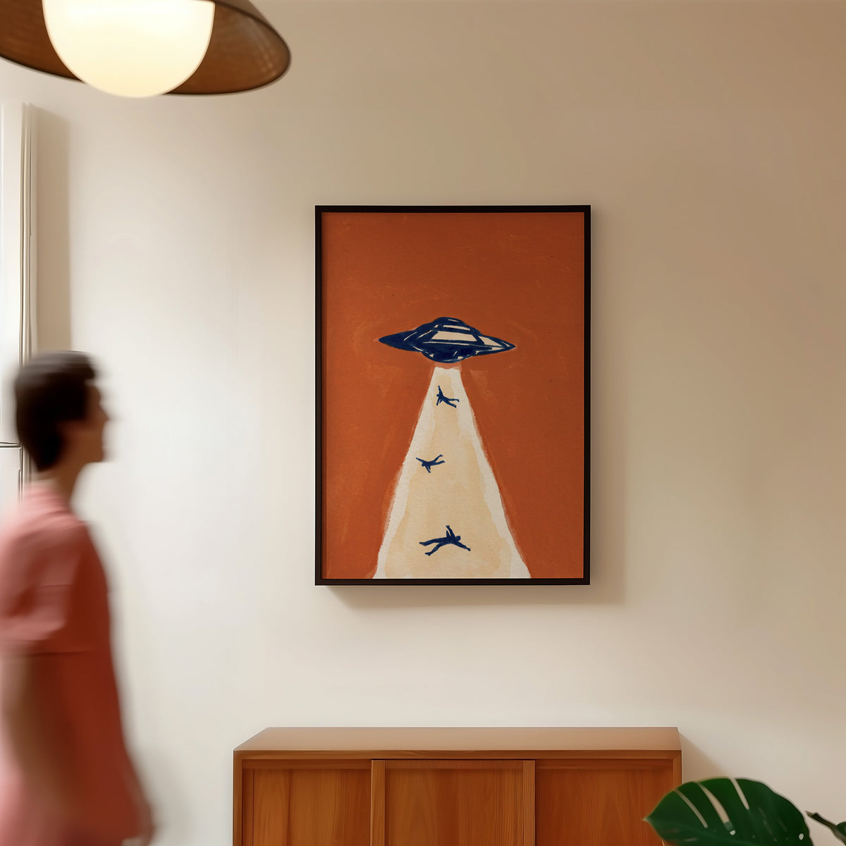 Rust and navy UFO print in a black frame in a hallway under a rattan pendant