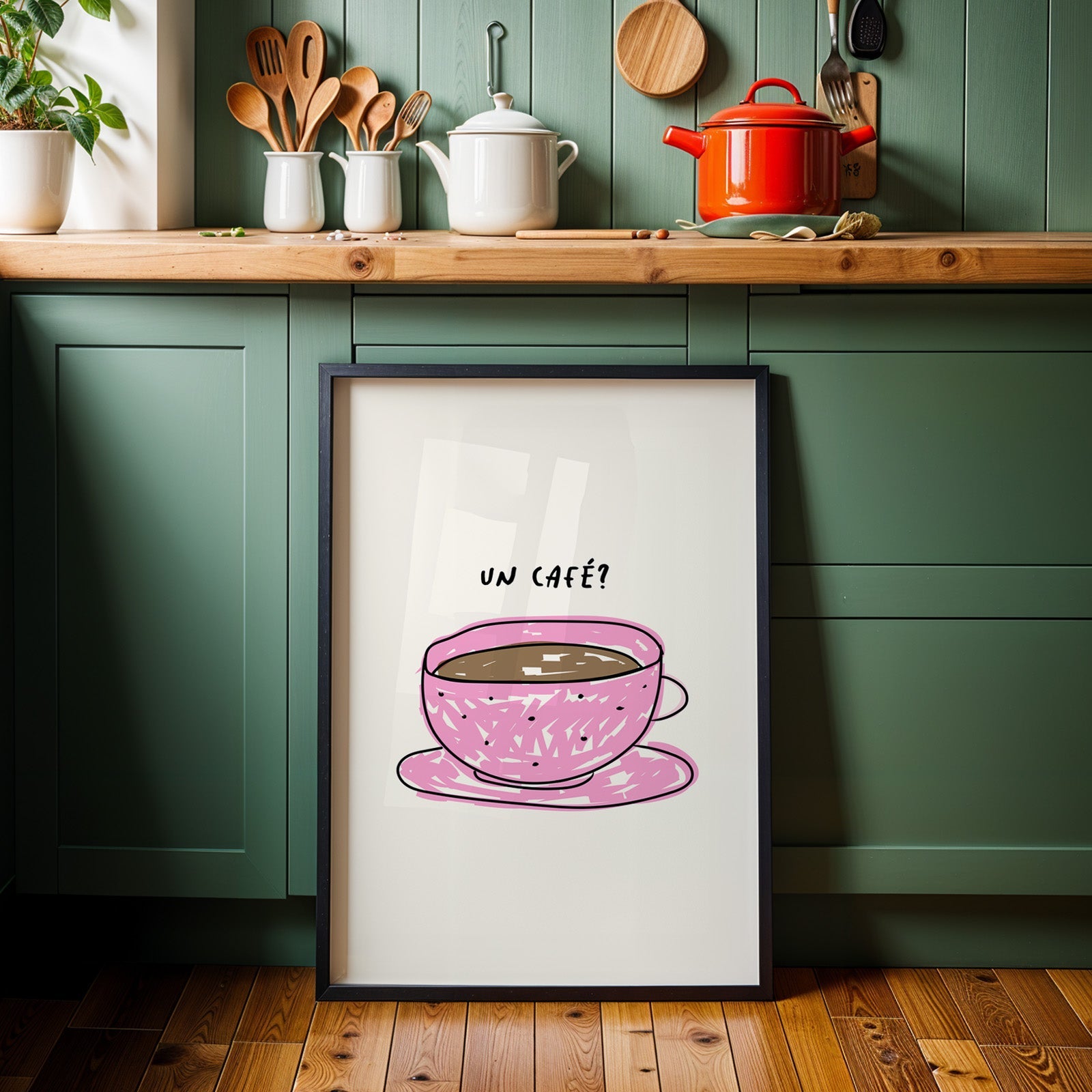 Un cafe pink cup print in a black frame against sage green kitchen cabinets