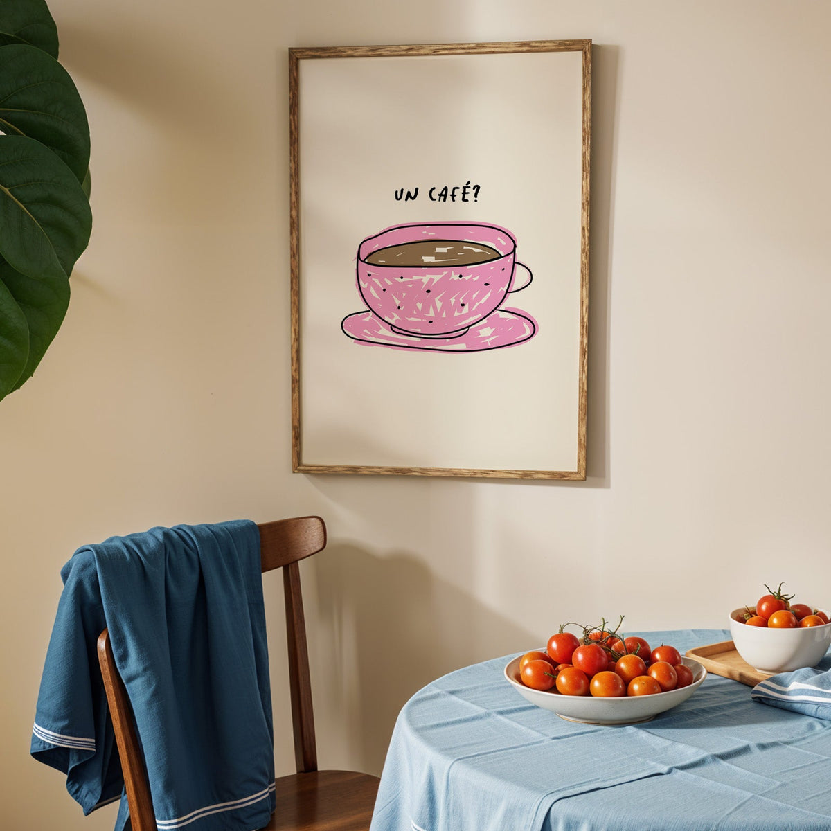Un cafe pink cup print in an oak frame above a blue linen table with ripe tomatoes