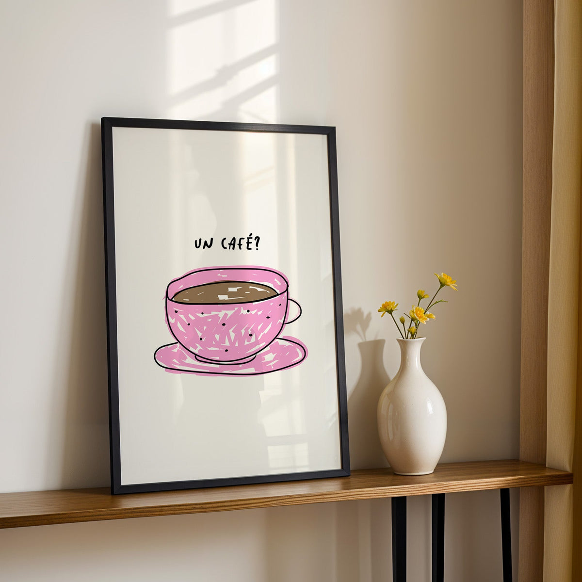 Un cafe pink cup print in a black frame on a console table with yellow daisies
