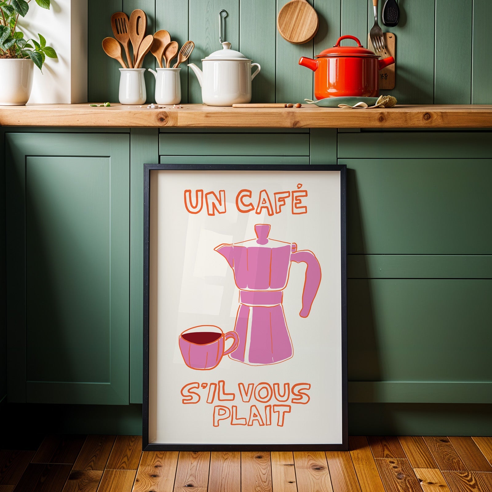 Un cafe pink moka pot print in a black frame against sage green kitchen cabinets