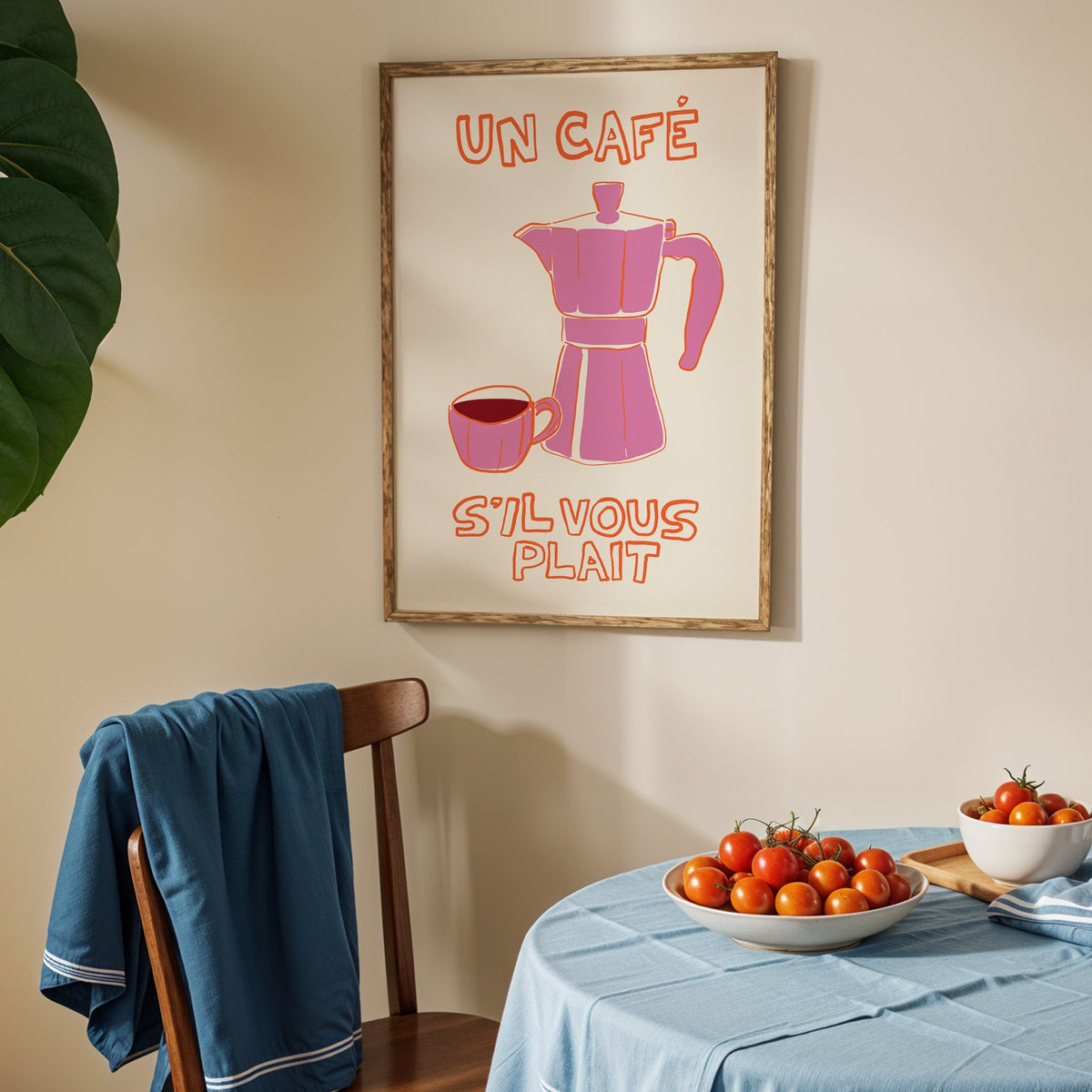 Un cafe pink moka pot print in an oak frame above a blue linen table with tomatoes