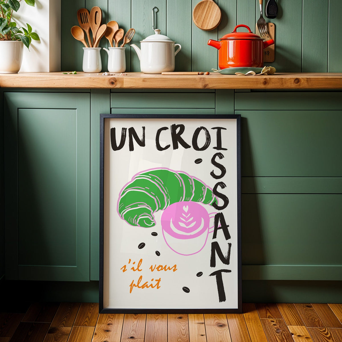 Un croissant french bakery print in a black frame against sage green cabinets