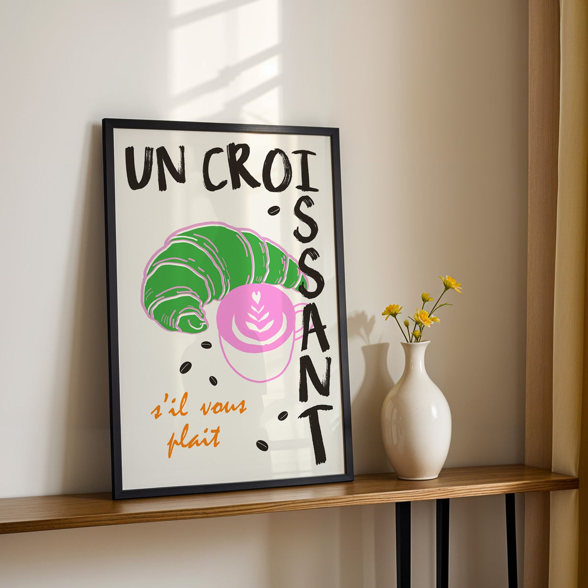 Un croissant french bakery print in a black frame on a console table with daisies