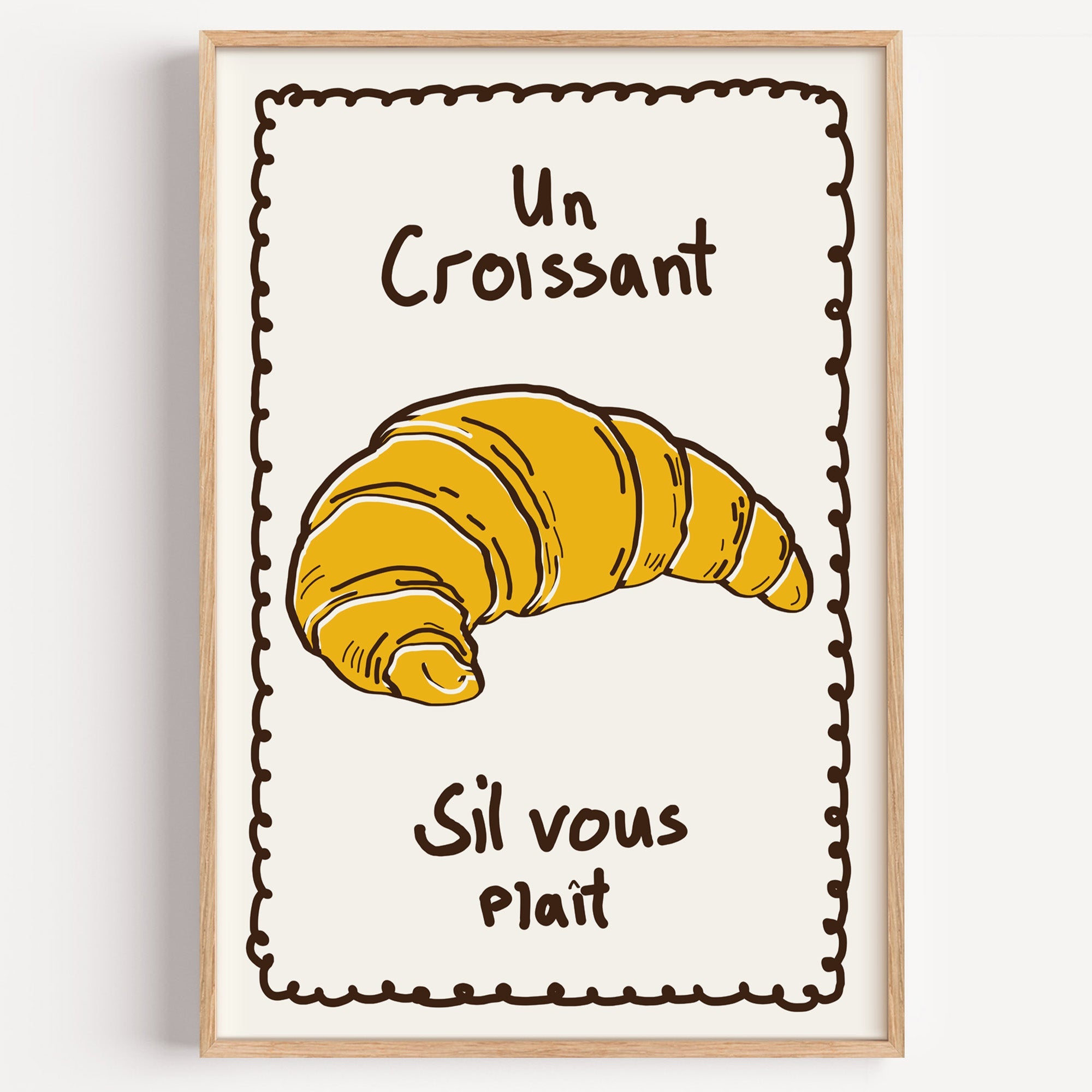 Un croissant yellow bakery print in a light oak frame on a plain white wall
