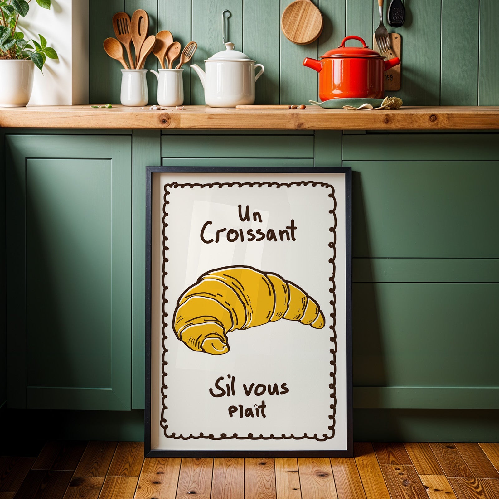 Un croissant yellow bakery print in a black frame against sage green cabinets