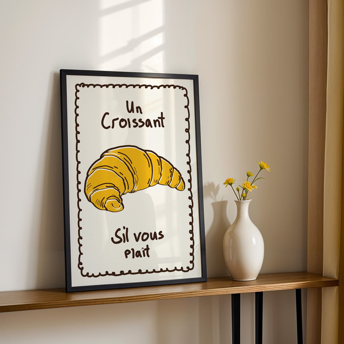Un croissant yellow bakery print in a black frame on a console table with daisies