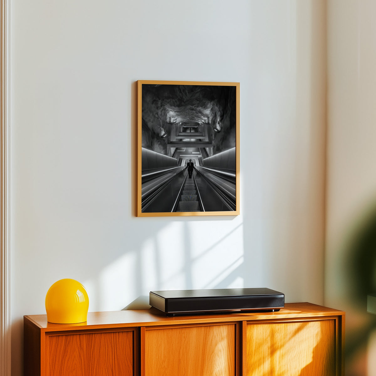 Black and white rock cave subway escalator print in an oak frame above a teak sideboard with a yellow glass lamp