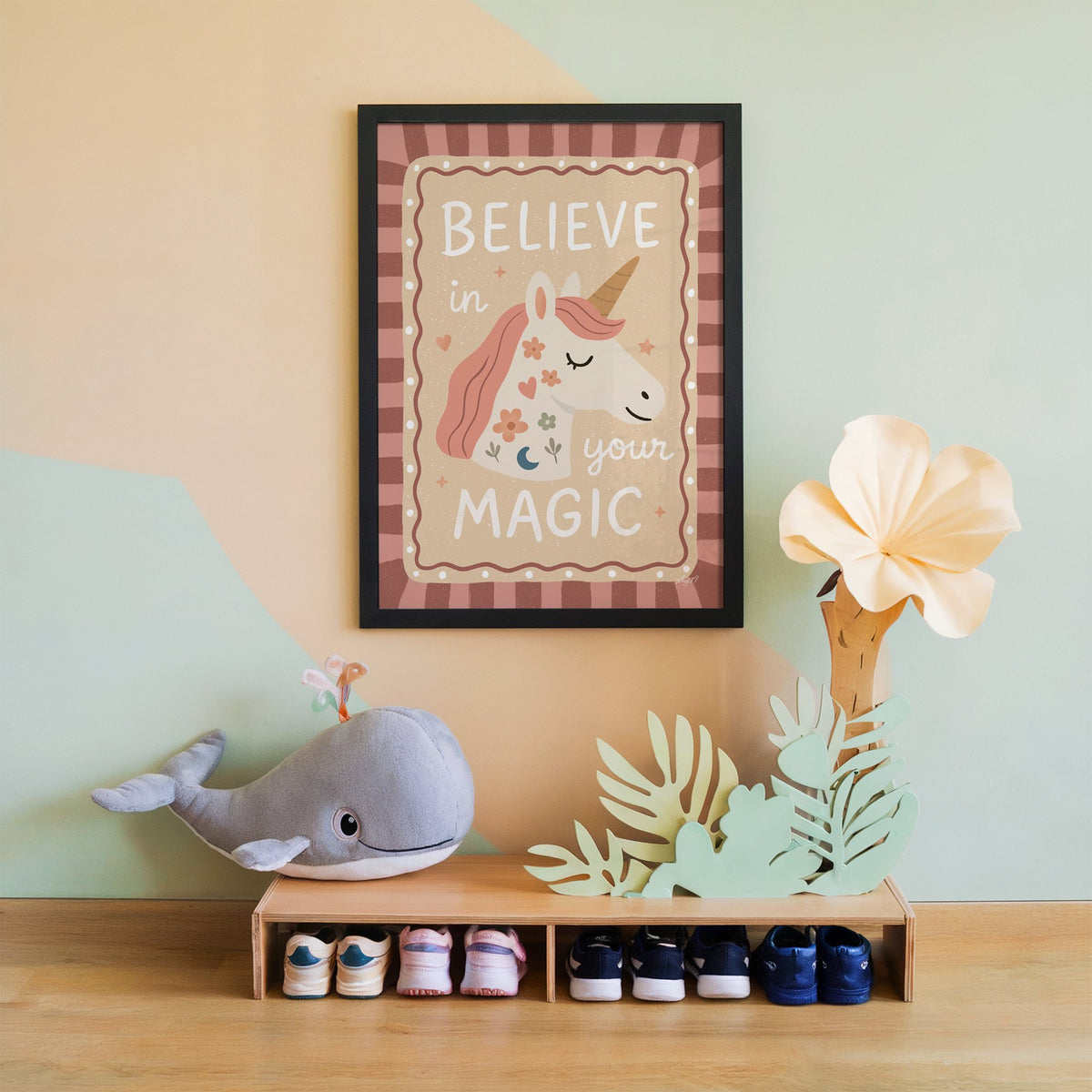 Unicorn head with magic quote nursery print in a black frame on a mint and peach wall above a whale plush