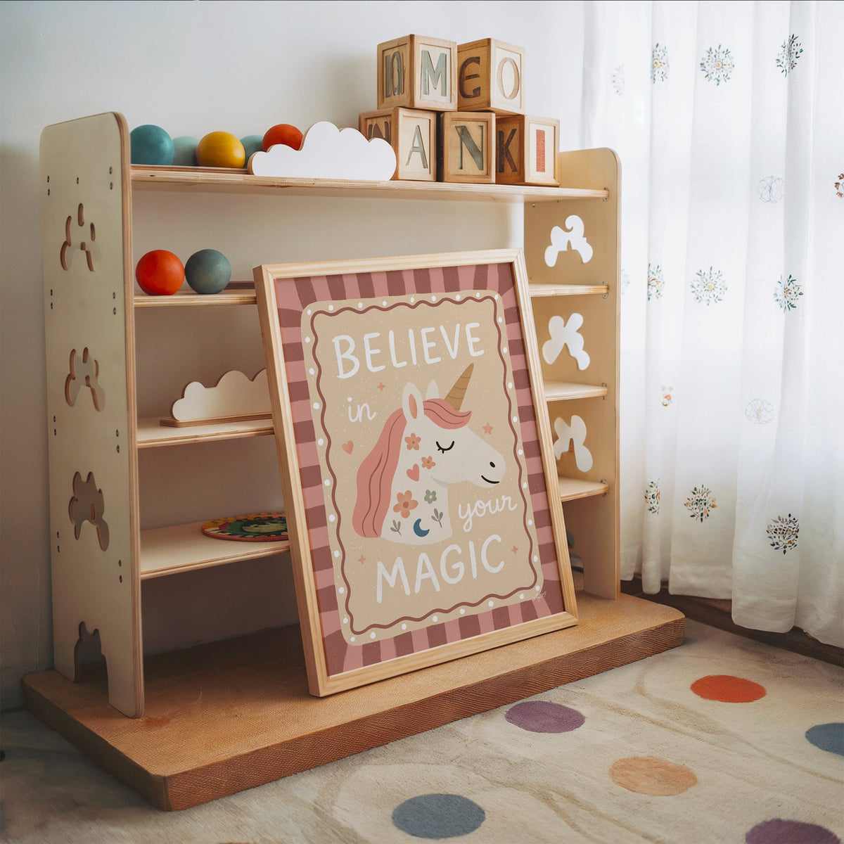 Unicorn head with magic quote nursery print in an oak frame leaning on a toy shelf with wooden letter blocks