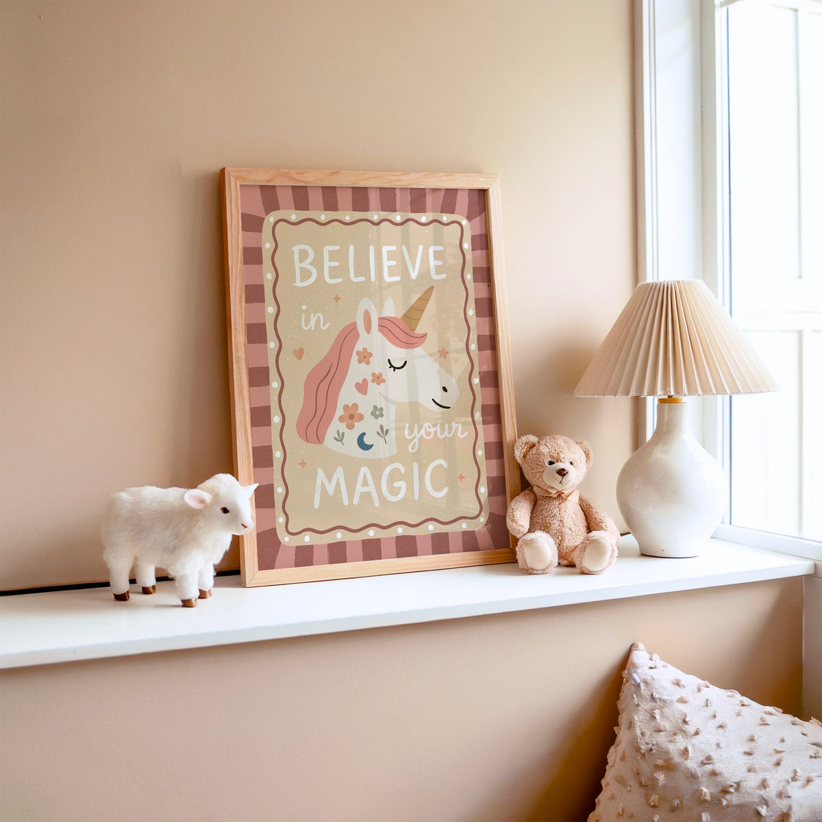 Unicorn head with magic quote nursery print in an oak frame on a window ledge with a toy lamb and teddy