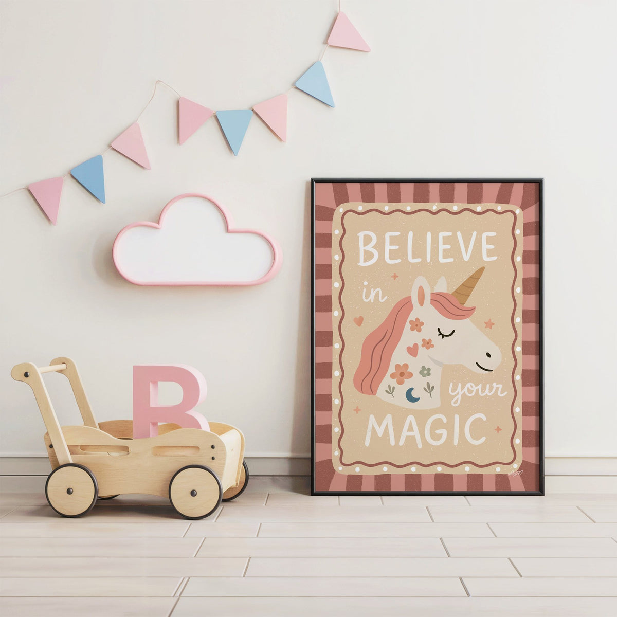 Unicorn head with magic quote nursery print in a black frame under pastel bunting by a wooden baby walker