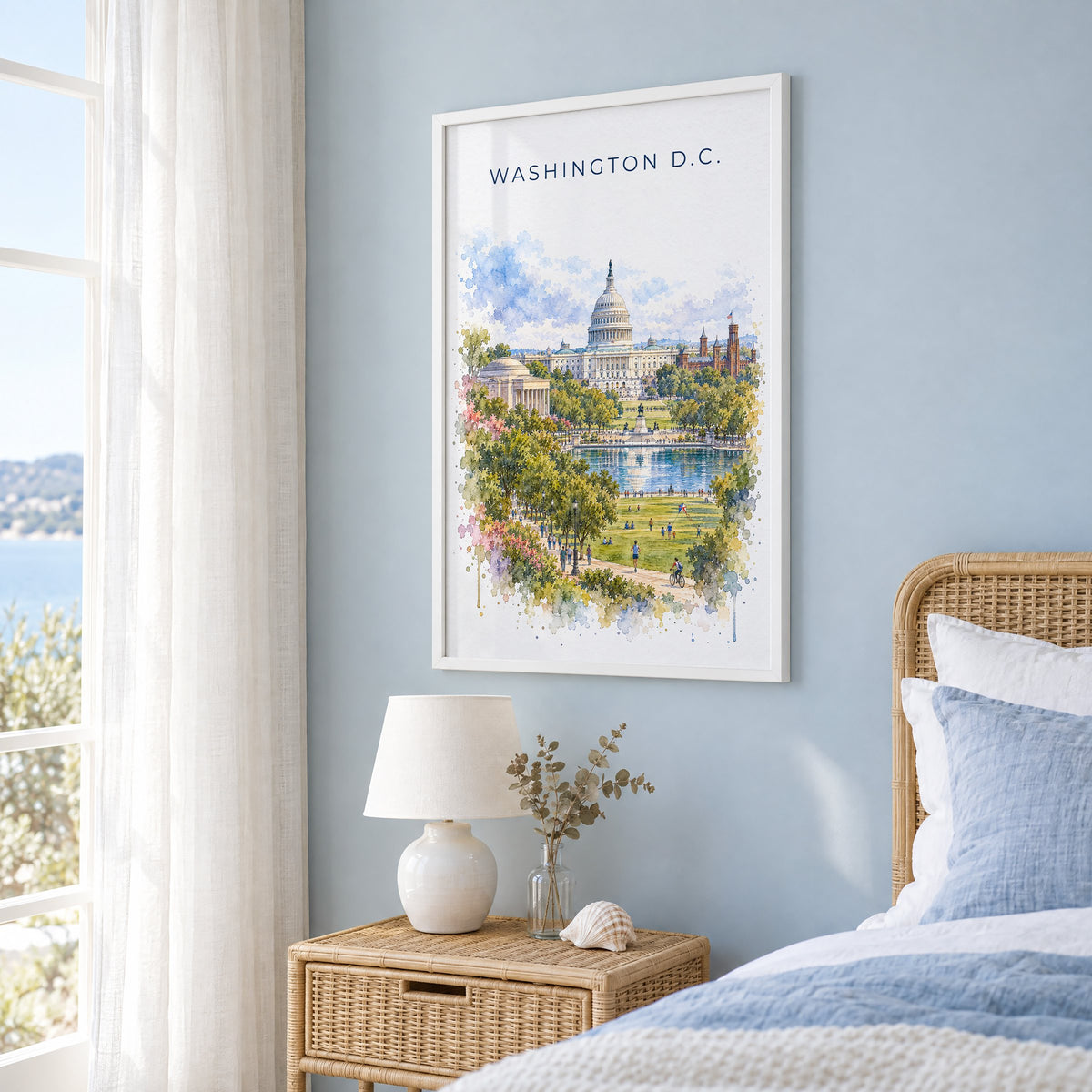 U.S. Capitol watercolor print in a white frame on a pale blue wall beside a rattan bed in a coastal bedroom