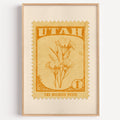 Utah state flower stamp print in orange gold on pale yellow, light oak frame on a plain white wall