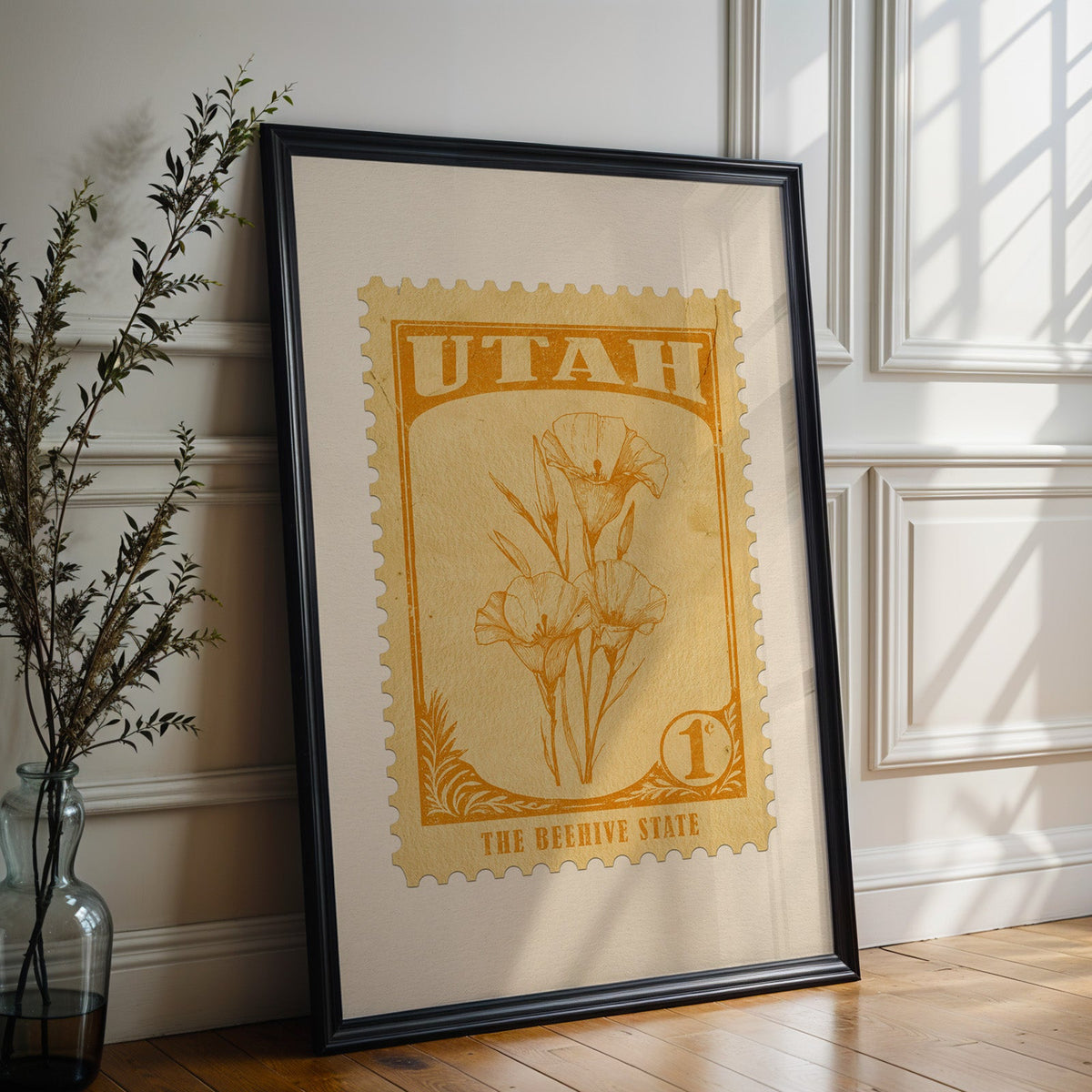 Utah state flower print in a black frame leaning against a white panelled wall beside olive branches