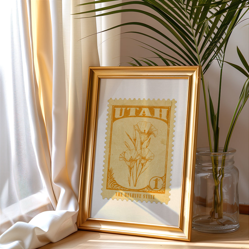 Utah stamp print in a gold frame leaning by a cream curtain with a palm in a glass jar