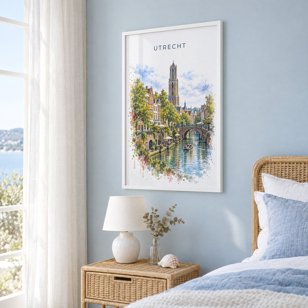Utrecht watercolor print in a white frame on a pale blue wall beside a rattan bed in a coastal bedroom