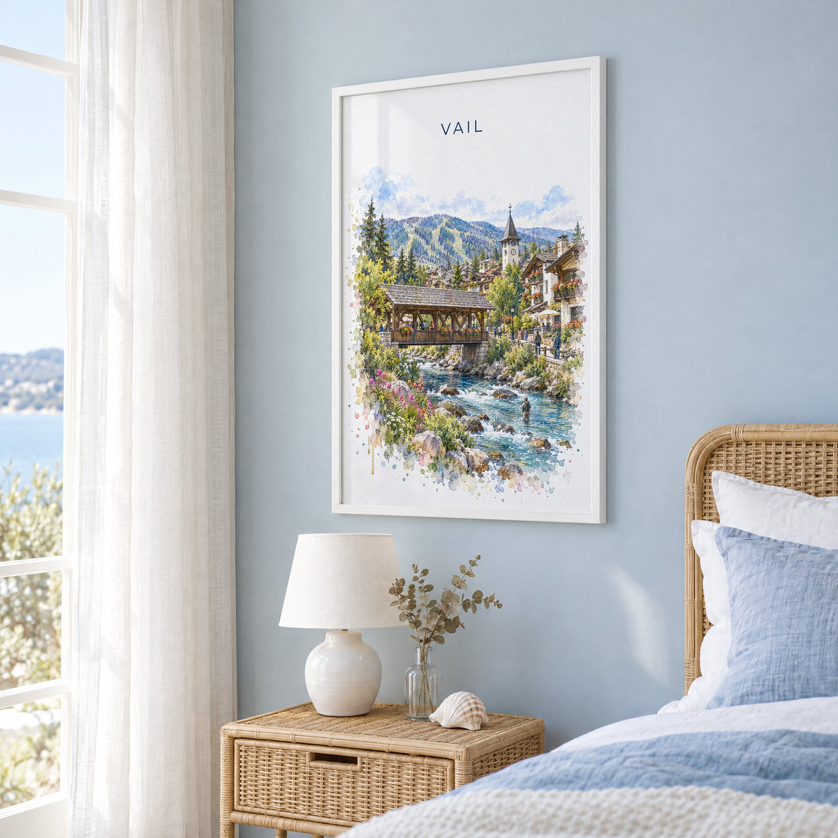 Vail, Colorado watercolor print in a white frame on a pale blue wall beside a rattan bed in a coastal bedroom