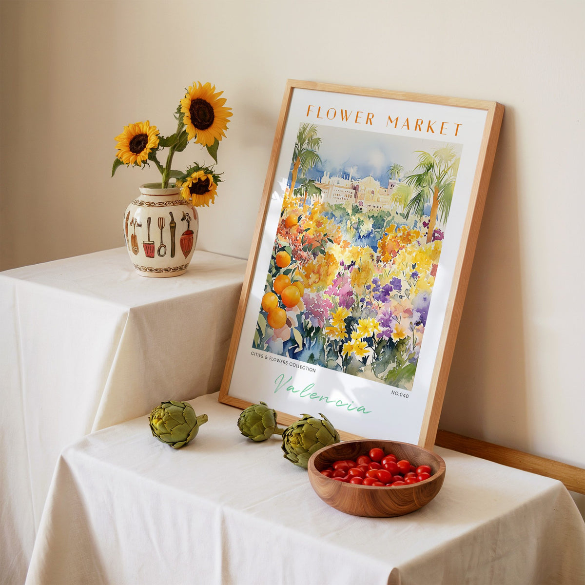 Valencia flower market print in an oak frame leaning on a linen-draped table beside a vase of sunflowers