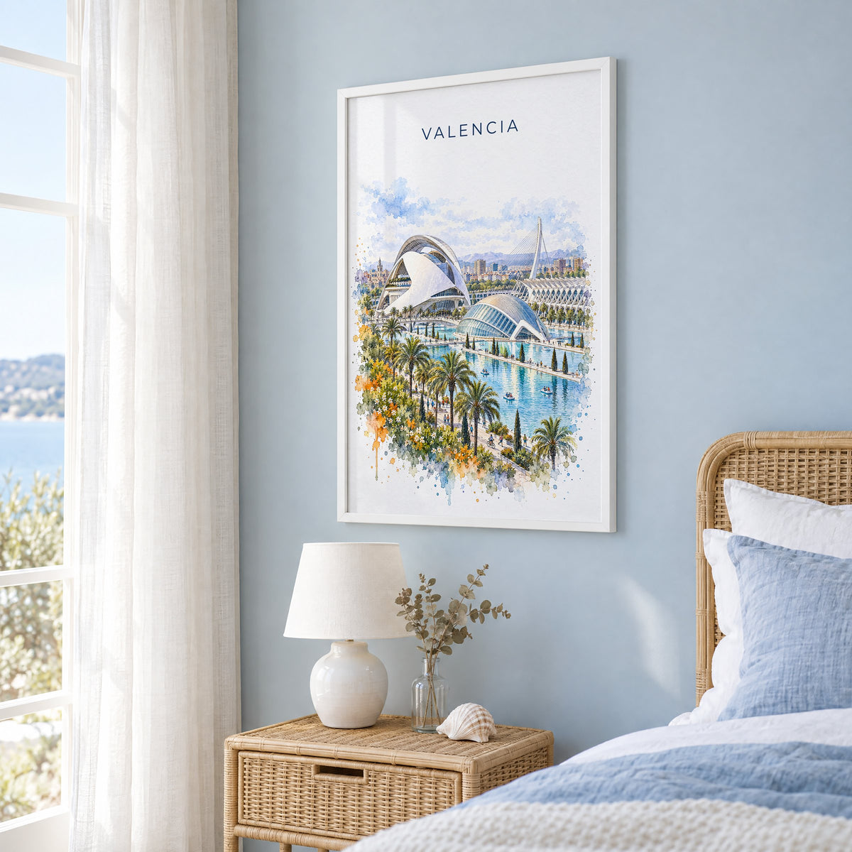 Valencia, Spain watercolor print in a white frame on a pale blue wall beside a rattan bed in a coastal bedroom