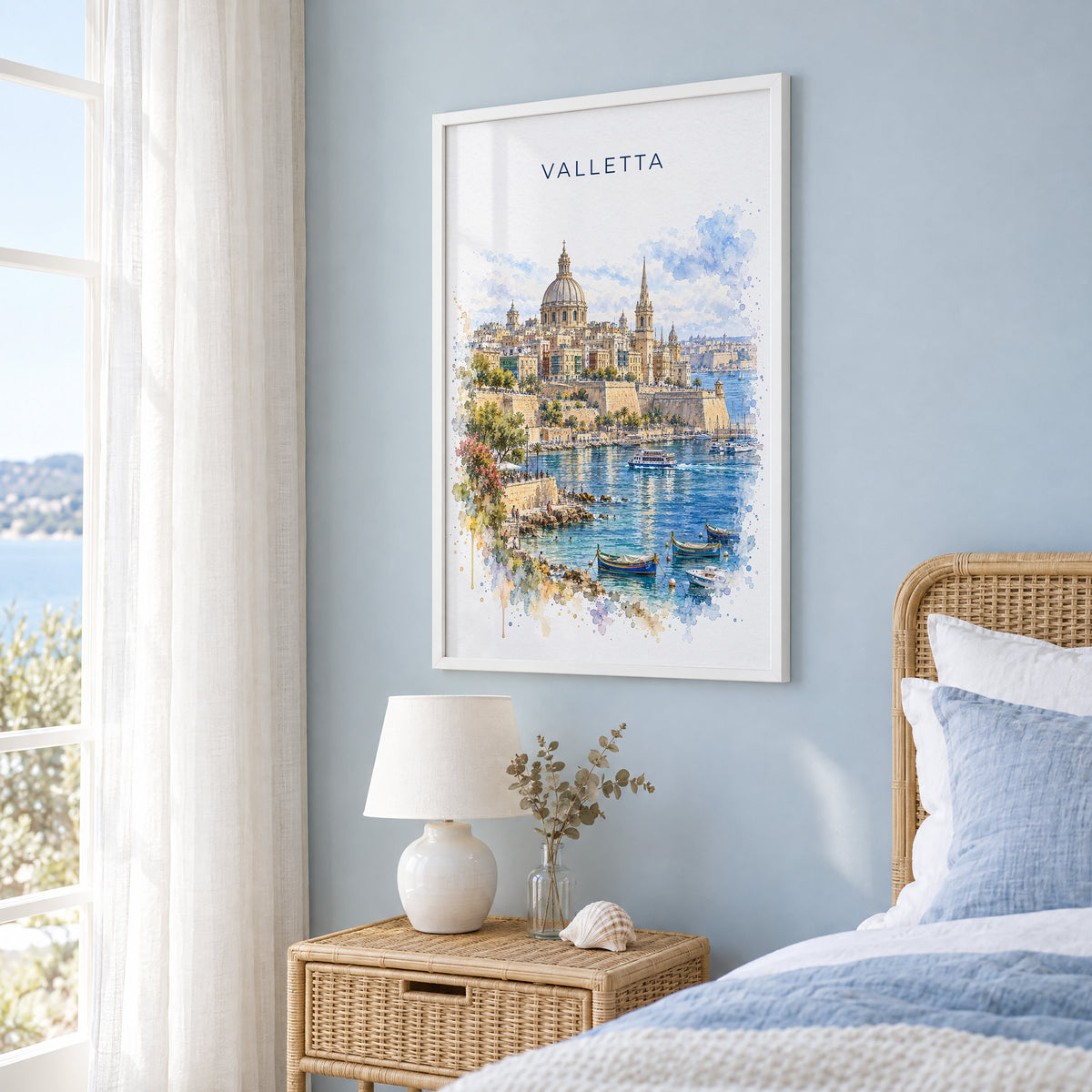 Valletta watercolor print in a white frame on a pale blue wall beside a rattan bed in a coastal bedroom