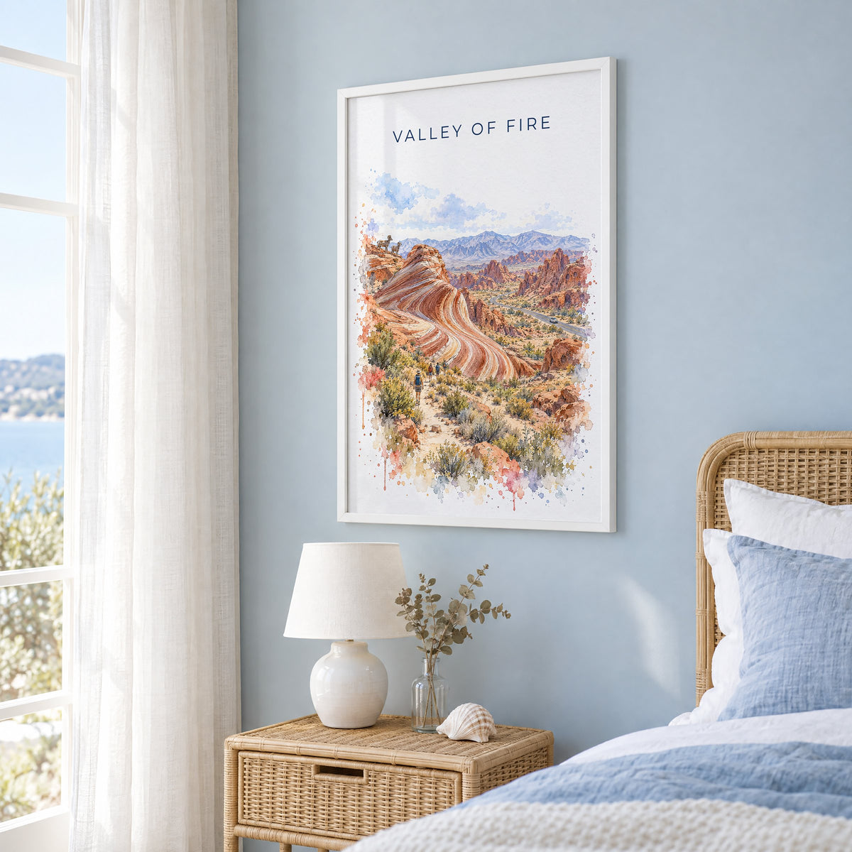 Valley of Fire watercolor print in a white frame on a pale blue wall beside a rattan bed in a coastal bedroom