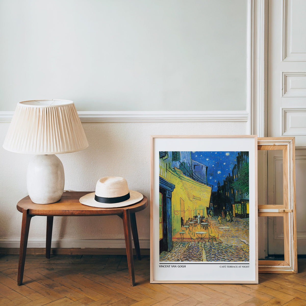 Van Gogh café terrace poster in a light wood frame leaning by a bench and panama hat