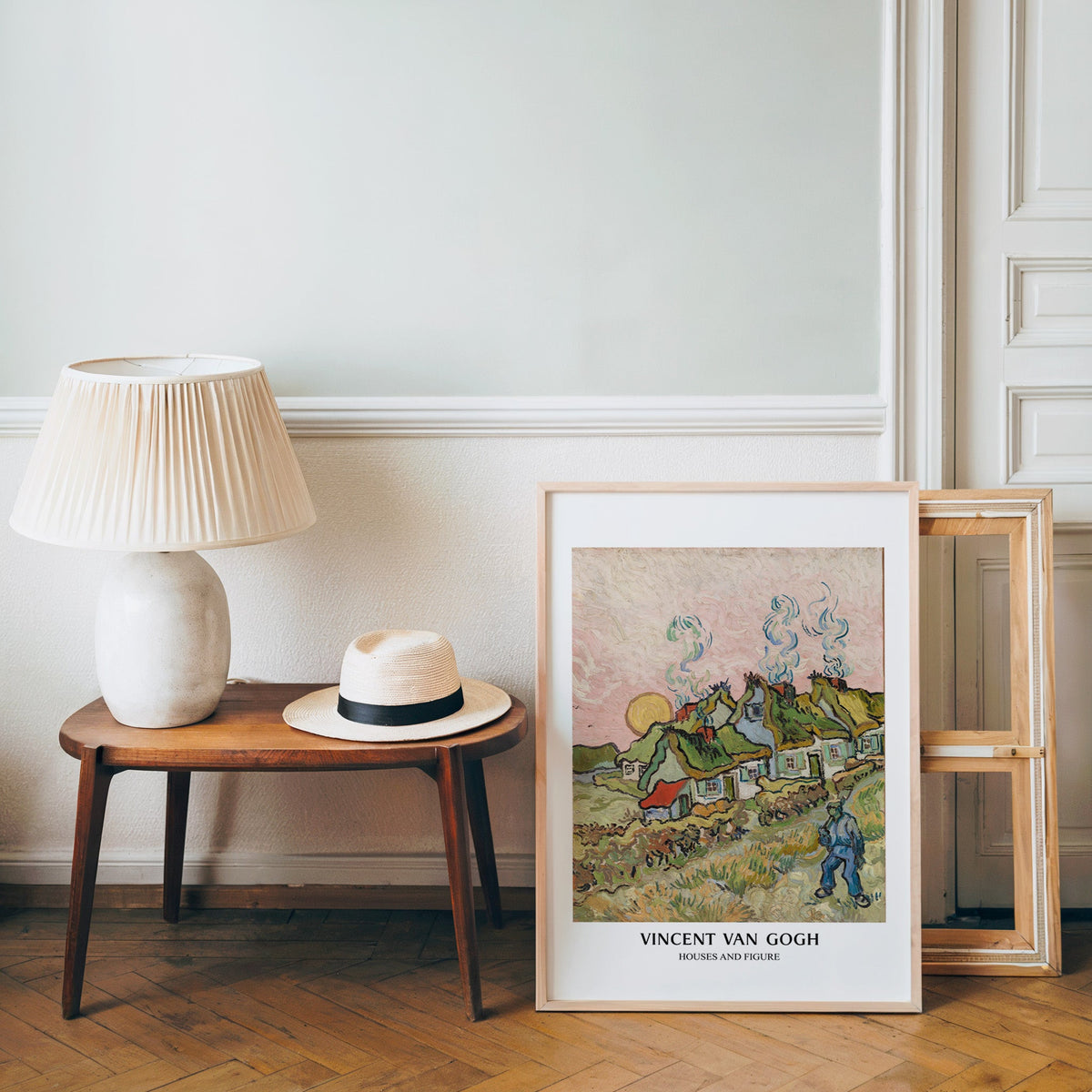 Van Gogh cottages poster in a light wood frame leaning by a bench and panama hat
