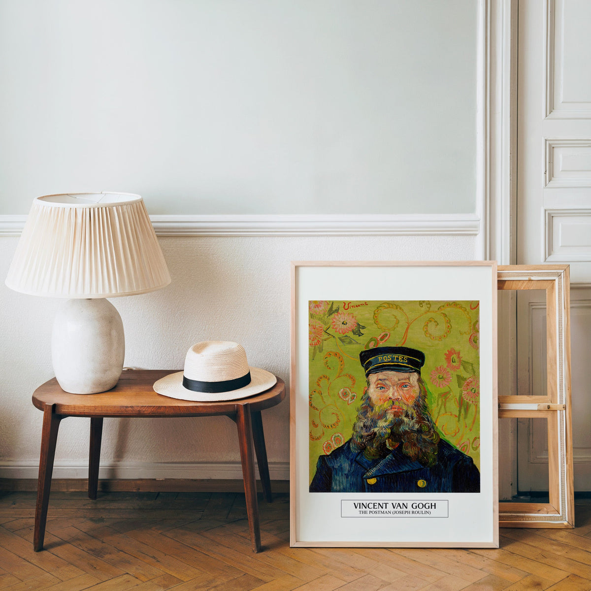 Van Gogh postman poster in a light wood frame leaning by a bench and panama hat