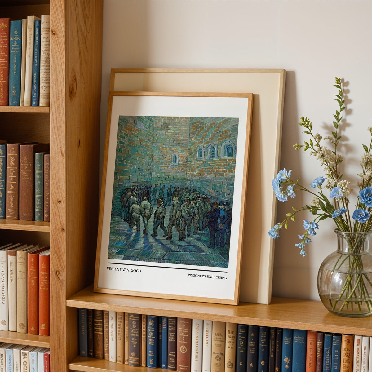 Van Gogh prison yard print in an oak frame leaning on a bookshelf beside blue flowers