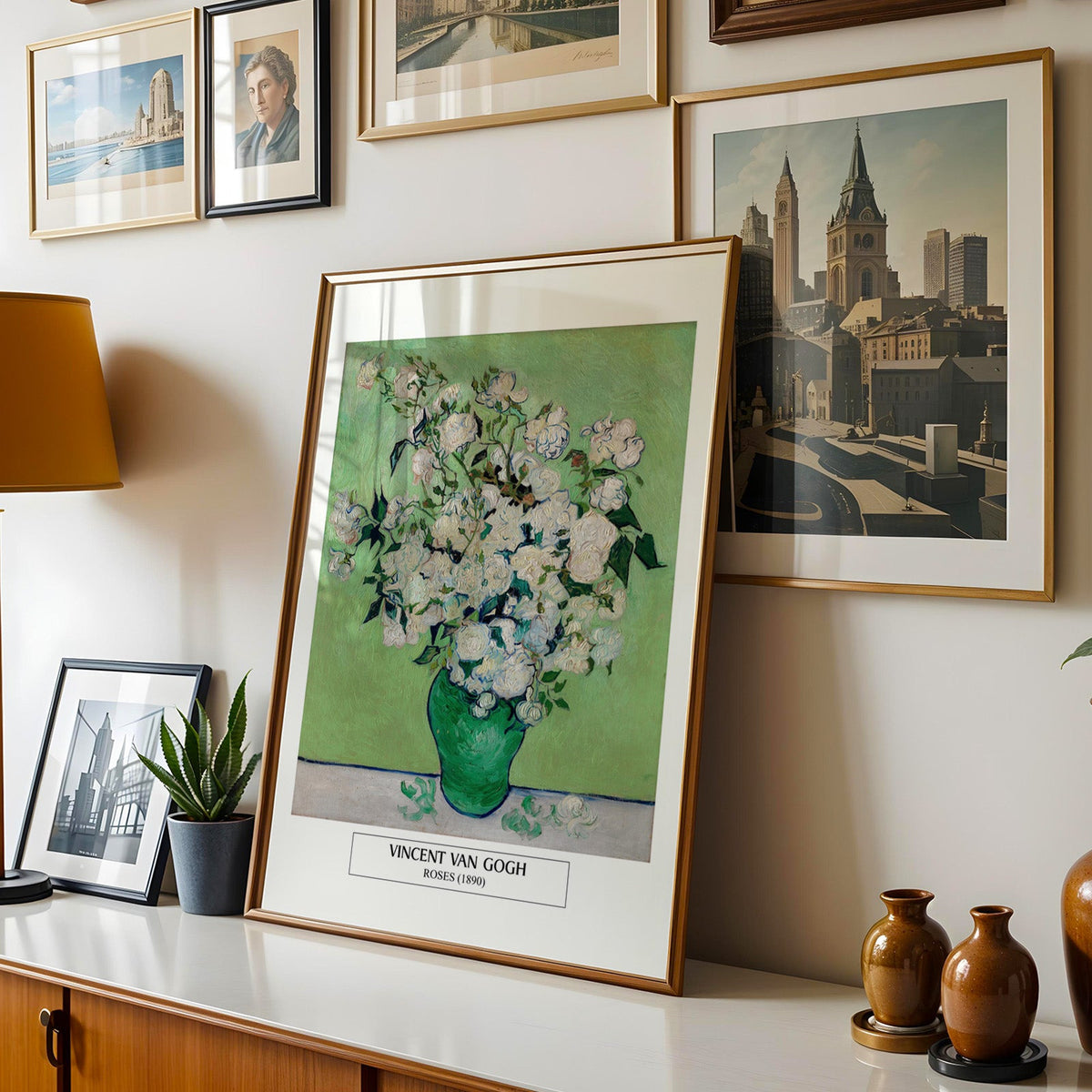 Van Gogh roses print shown in a gold frame leaning on a sideboard in a gallery wall
