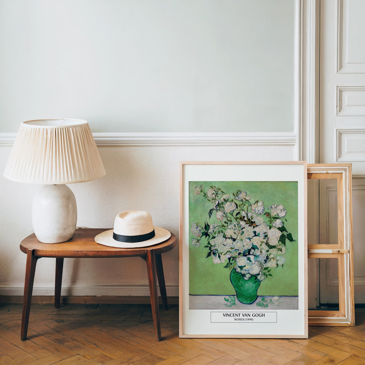 Van Gogh roses poster in a light wood frame leaning by a bench and panama hat