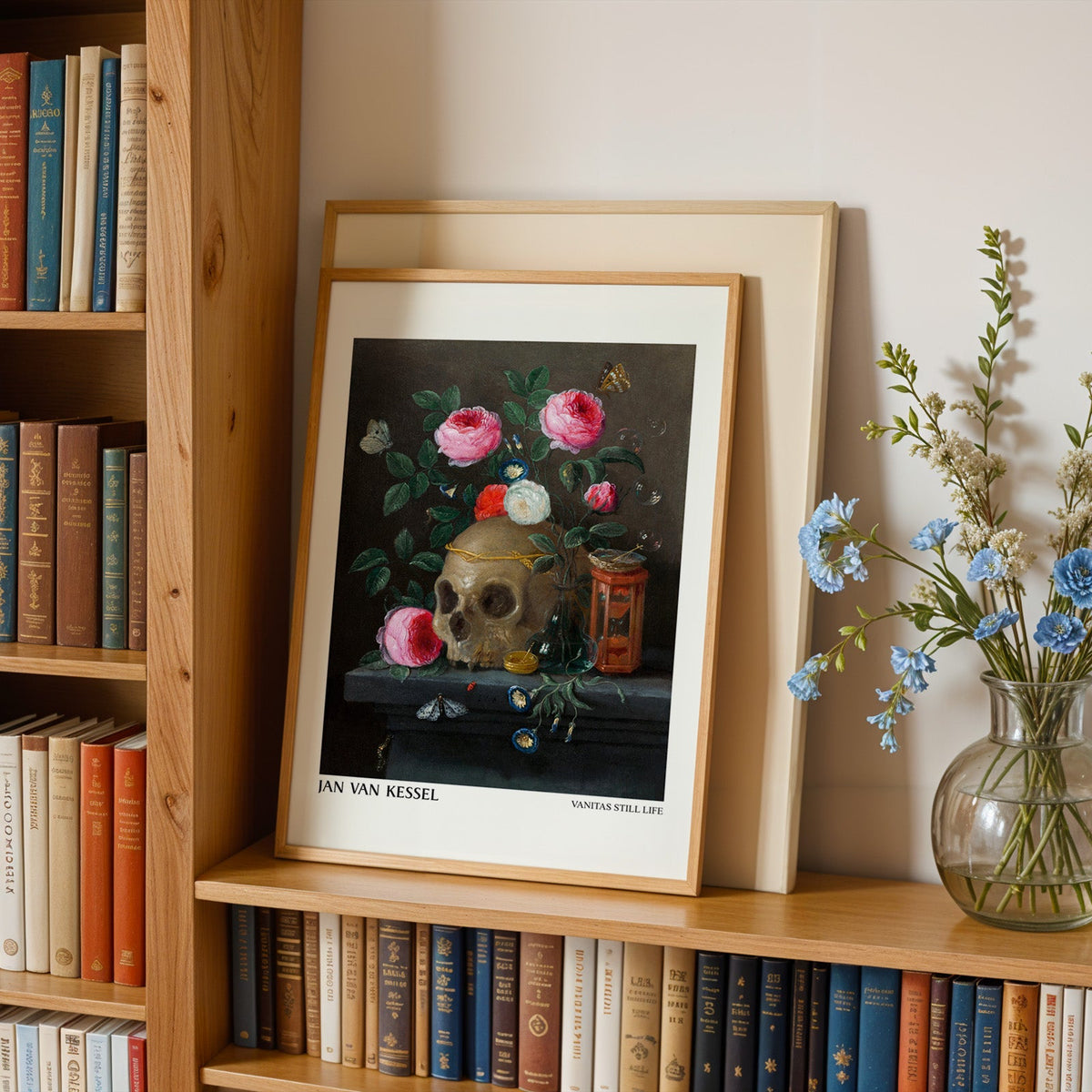 Rose and skull painting print in an oak frame leaning on a bookshelf beside flowers